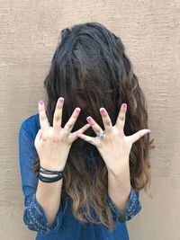 Young woman showing nail polish while standing against wall