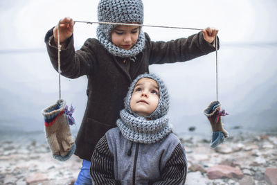 Girl in knitted grey hat sharing gloves with her frozen brother