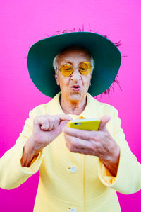 Senior woman using phone against pink background