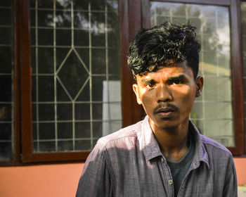 Portrait of young man standing against window