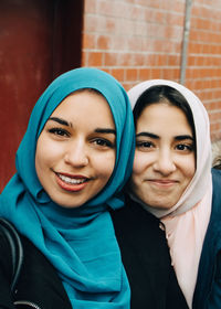 Portrait of smiling young woman taking with teenage friend against building in city