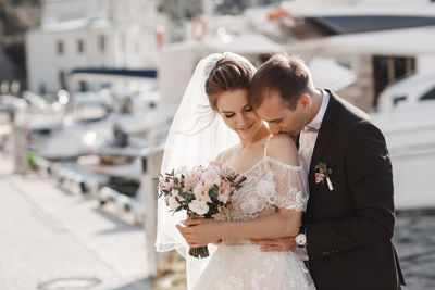 Newlywed couple embracing while standing at harbor