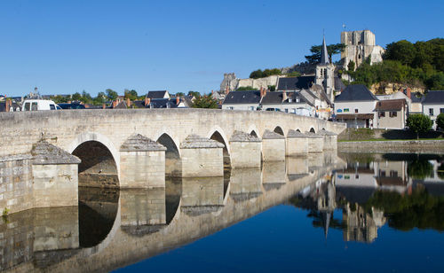 Arch bridge over river by buildings against sky