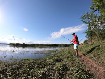 Full length of man fishing on lake against sky