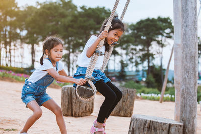 Side view of girl pushing sister on swing at playground