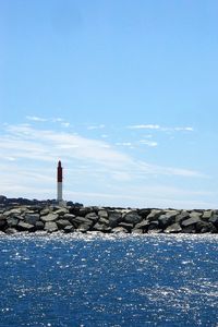 Lighthouse by sea against blue sky