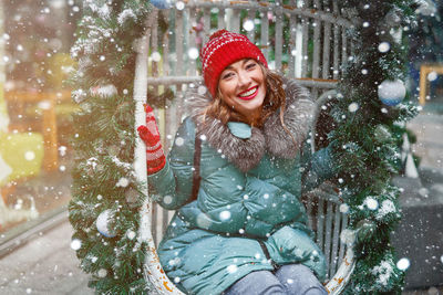 Portrait of smiling woman in snow sitting on swing outdoors