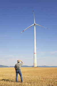 Farmer looking at a huge windmill in his farmland on a sunny day