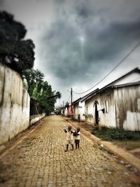 People walking on footpath by street against sky