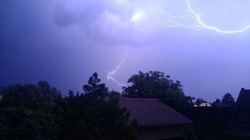 Low angle view of lightning over trees against sky at night