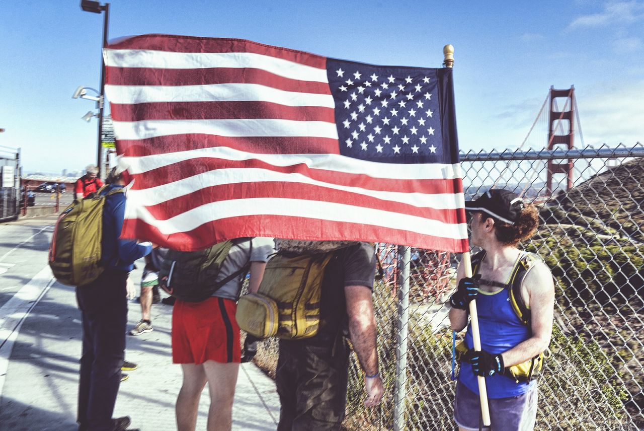 PEOPLE WALKING IN FRONT OF RED FLAG AGAINST CLEAR SKY