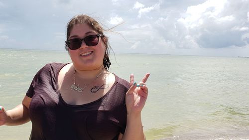 Portrait of smiling woman gesturing peace sign against sea