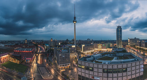 Fernsehturm in illuminated cityscape against cloudy sky at dusk