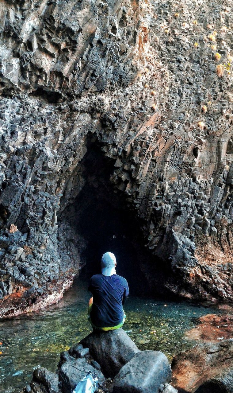 REAR VIEW OF SENIOR MAN SITTING ON ROCK