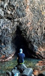 Rear view of man sitting on rock