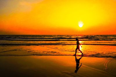 Silhouette person standing on beach against orange sky