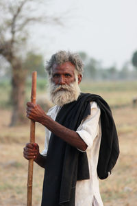 Portrait of senior bearded man holding cane while standing on field
