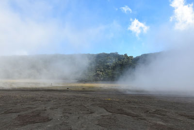 Smoke emitting from volcanic landscape against sky