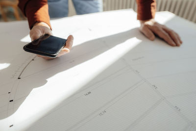 Hand of businessman holding mobile phone on blueprint in office