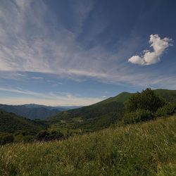 Scenic view of green mountains against cloudy sky on sunny day