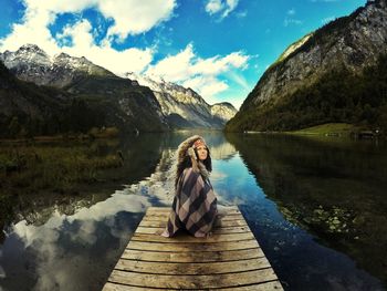 Woman sitting by lake against sky