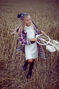 Blonde girl in white in a dress and boots goes with a dream catcher in a wheat field