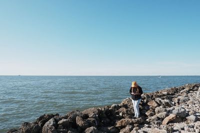 A woman stands on a rock on the edge of a calm sea shore