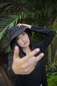 Portrait of young woman wearing hat standing against plants