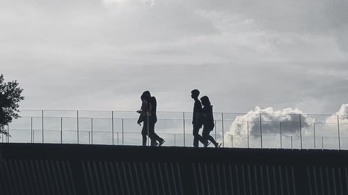 Man and woman standing on railing against sky