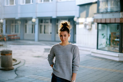 Portrait of young woman standing against building on street in city