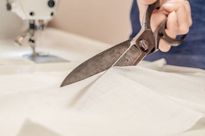 The dressmaker cuts the white cloth on table