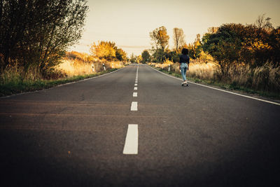 Rear view of young woman skateboarding on road against sky