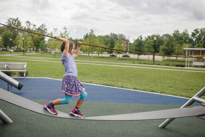 A little girl balances on playground equipment outside in summertime