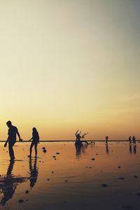 Silhouette people on beach against sky during sunset