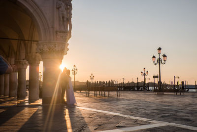 Couple standing by column on street during sunset