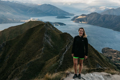 Portrait of young woman standing on rock against sky