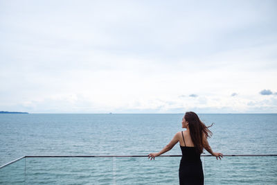 Rear view of woman standing at sea against sky