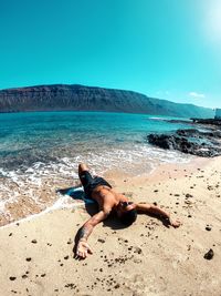 Full length of shirtless man at beach against sky