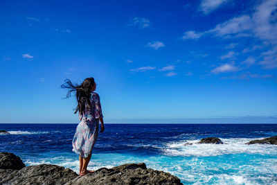 Woman on rock by sea against blue sky