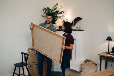 Man and woman looking at painting while standing by fireplace in living room