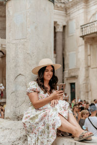 Woman sitting outside leaning against column using cell phone at busy city square in split, croatia