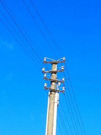 Low angle view of electricity pylon against blue sky