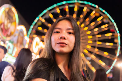 Portrait of young woman in illuminated carousel at amusement park