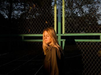 Full length of woman standing by fence against trees