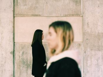 Side view of young women standing against wall