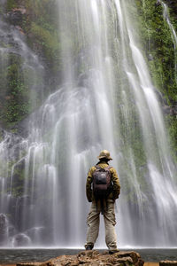 Rear view of man standing against waterfall at forest