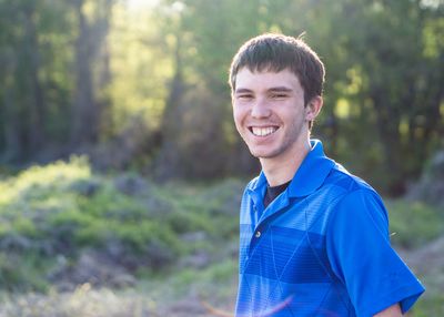 Portrait of happy young man standing against trees in forest