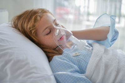 Girl wearing oxygen mask while lying on bed in hospital ward