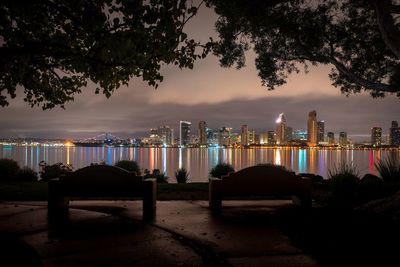 Illuminated city by river against sky at dusk