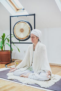 Mature female with closed eyes sitting with crossed legs on fluffy rug while practicing yoga at home